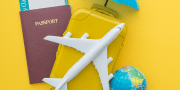 Campagne vakantiegevoel; afbeelidng van paspoort, vliegtuig, wereldbol, koffer en verzekeringsparaplu op een gele achtergrond
